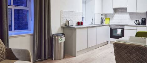 A modern kitchen with white cabinets, a stainless steel trash bin, and a window with curtains.