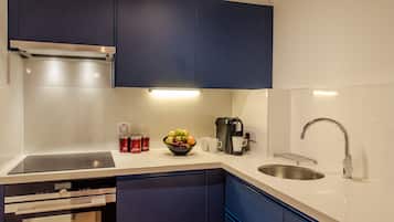 A modern kitchen with dark blue cabinets, a stainless steel sink, a built-in oven, and a coffee maker.