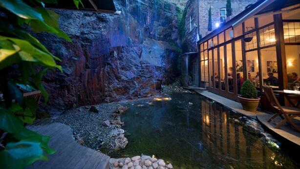 Uma fonte interior tranquila, com um cenário rochoso e um deck de madeira.