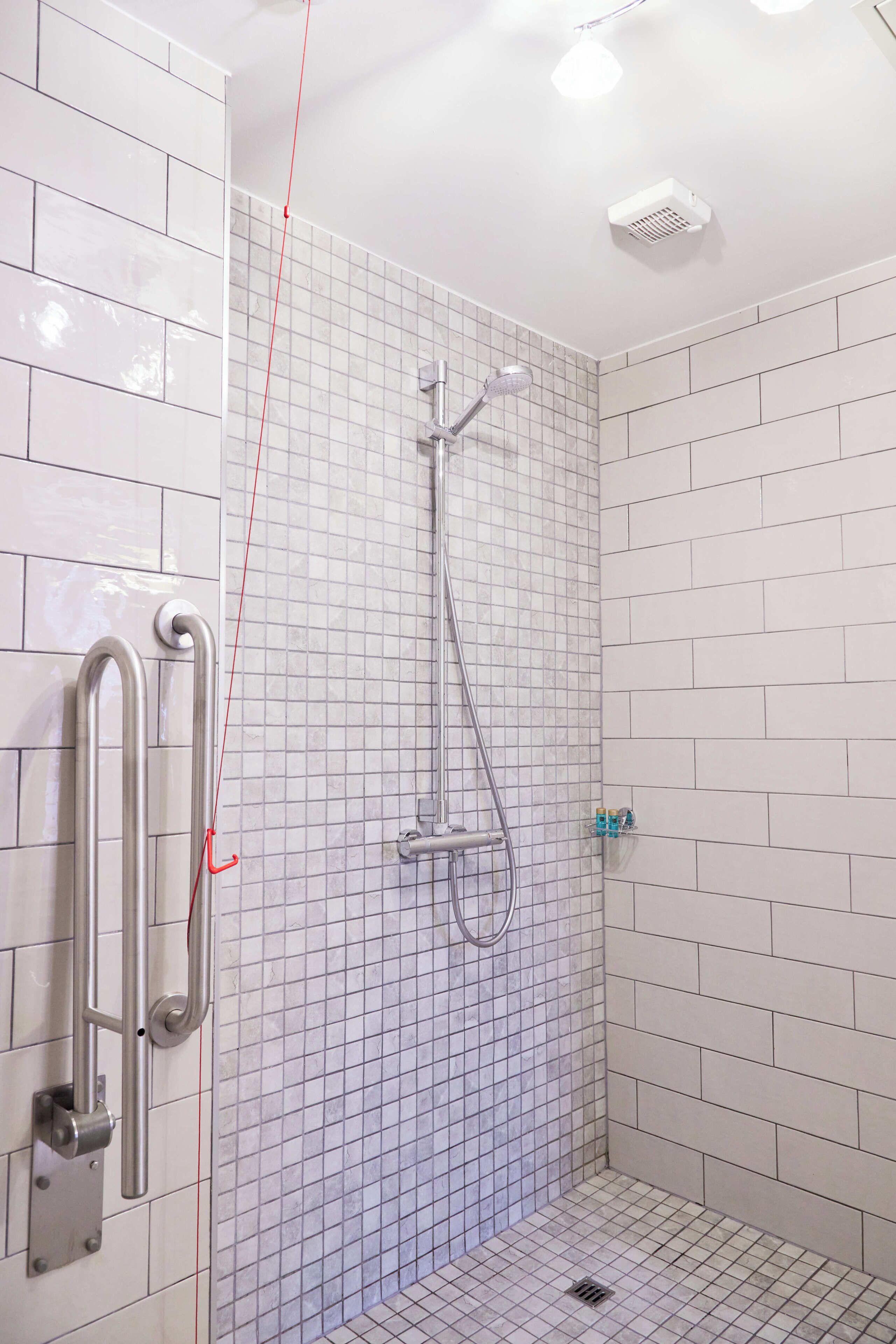 A small, tiled shower room with a handheld showerhead and a wall-mounted faucet.