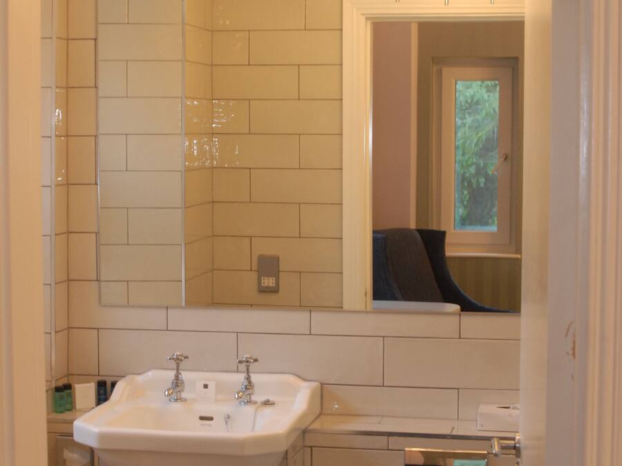 Un baño con un lavamanos blanco, espejo y retrete. Hay una ventana sobre el retrete y una araña de cristal sobre el lavamanos.