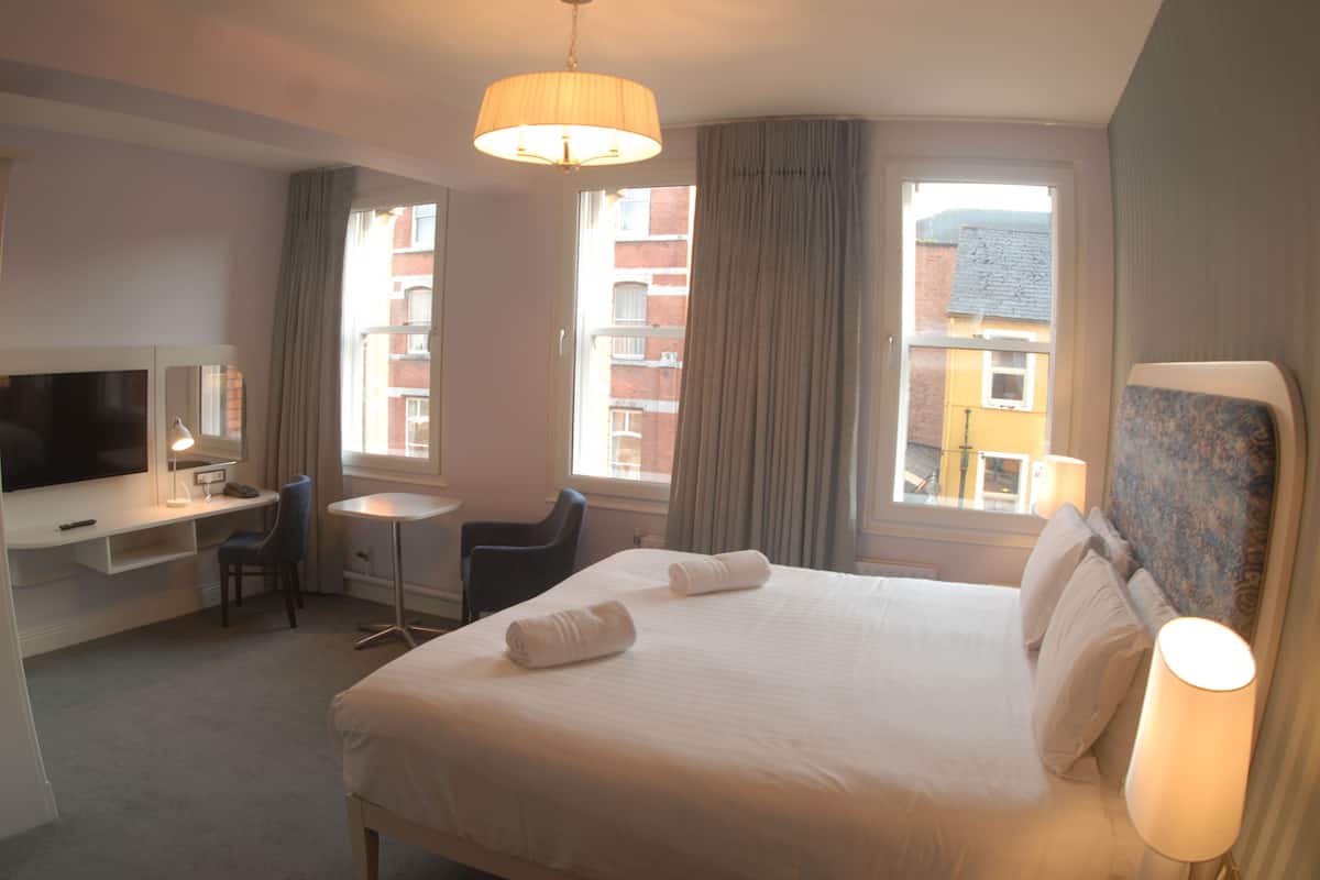 A hotel room with a bed, a desk, a chair, a television, and a window with curtains.