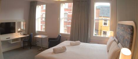 A hotel room with a bed, a desk, a chair, a television, and a window with curtains.