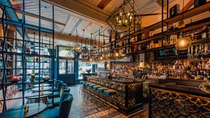 Uma área de bar com um balcão comprido, vários bancos e prateleiras cheias de garrafas.