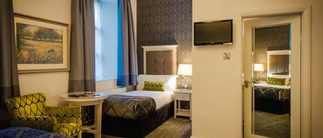Une chambre d’hôtel avec un lit, une chaise, une petite table, un téléviseur et une porte donnant sur une autre pièce.