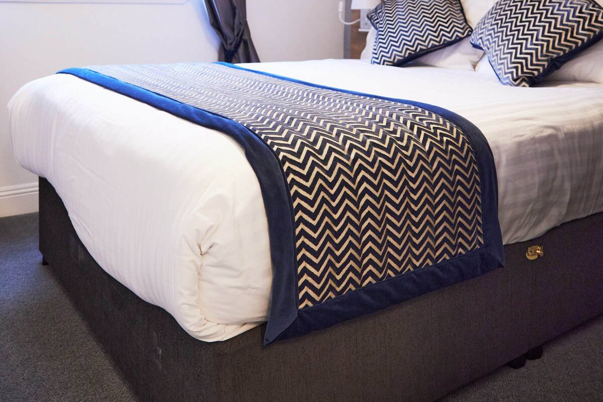 A neatly made bed with a blue and black patterned throw, a wooden headboard, and two matching pillows.