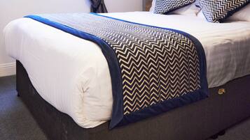 A neatly made bed with a blue and black patterned throw, a wooden headboard, and two matching pillows.