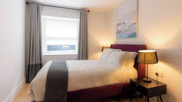 Una cama bien hecha con cabecera, lámpara de noche y ventana con cortinas.