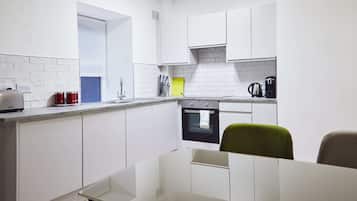 Una cocina moderna con armarios blancos, horno empotrado y cafetera.
