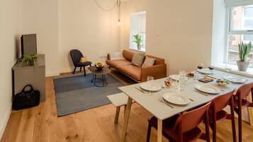 A modern living room with a sofa, a dining table set for four, and a small side table with a plant.