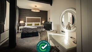 Quarto de hotel com cama, televisão, escrivaninha e espelho.