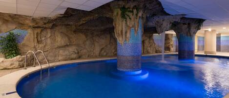 Una piscina interior con una estructura tipo cueva rocosa y un pilar con azulejos.