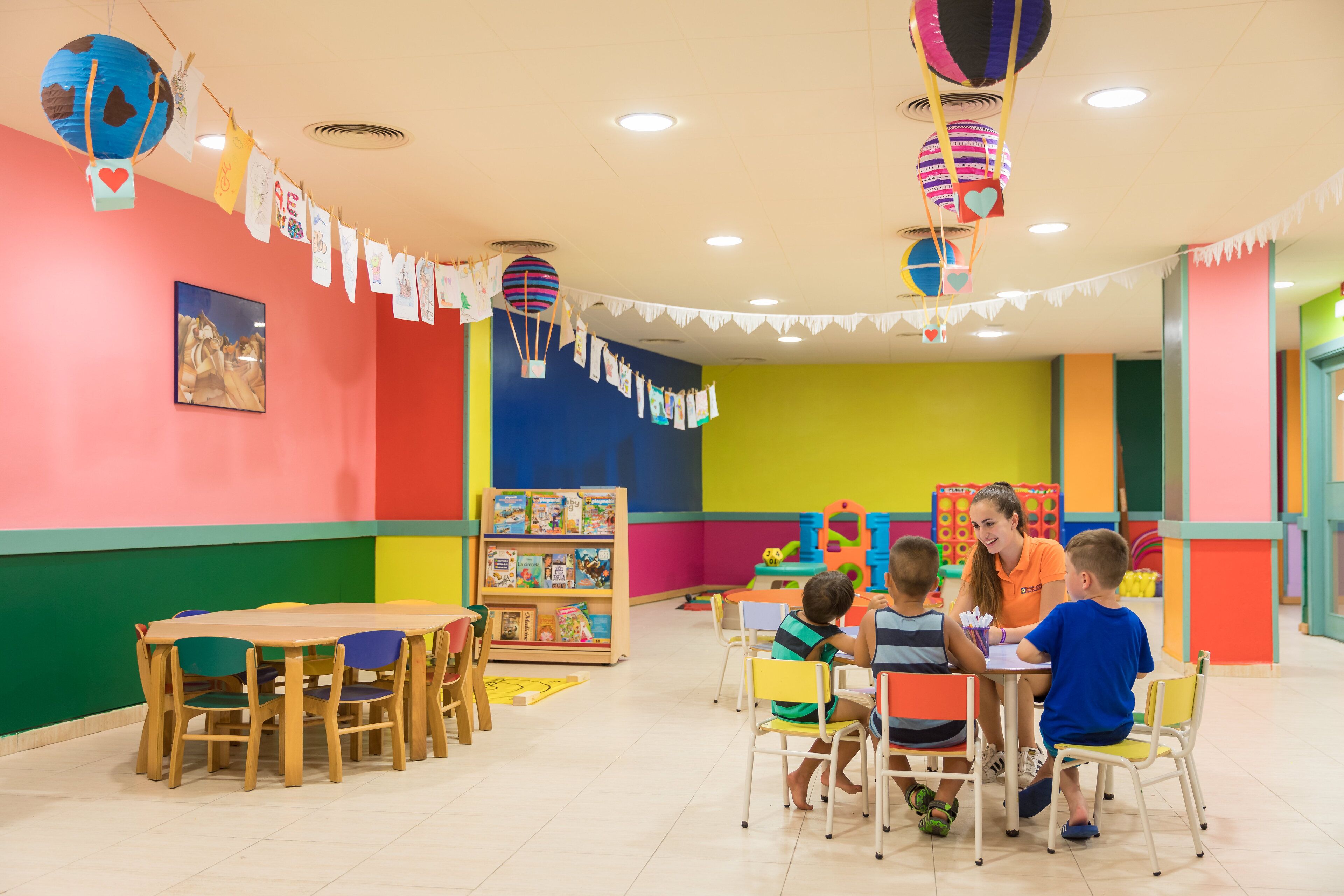 A brightly colored children's playroom with a table and chairs, a bookshelf, and hanging decorations.