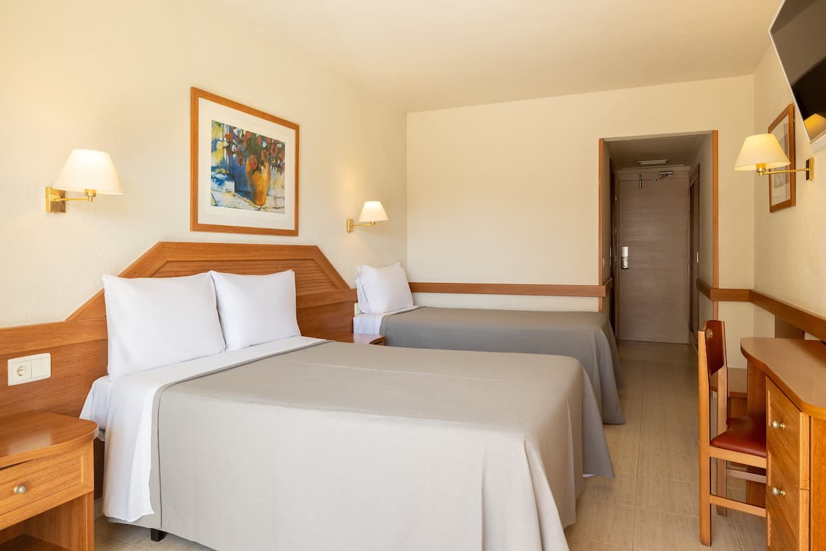 Una habitación de hotel con dos camas, un escritorio de madera, una silla y una puerta que da a otra habitación.