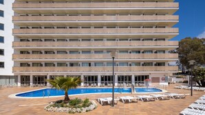 Un hotel con varias plantas, piscina al aire libre y tumbonas.