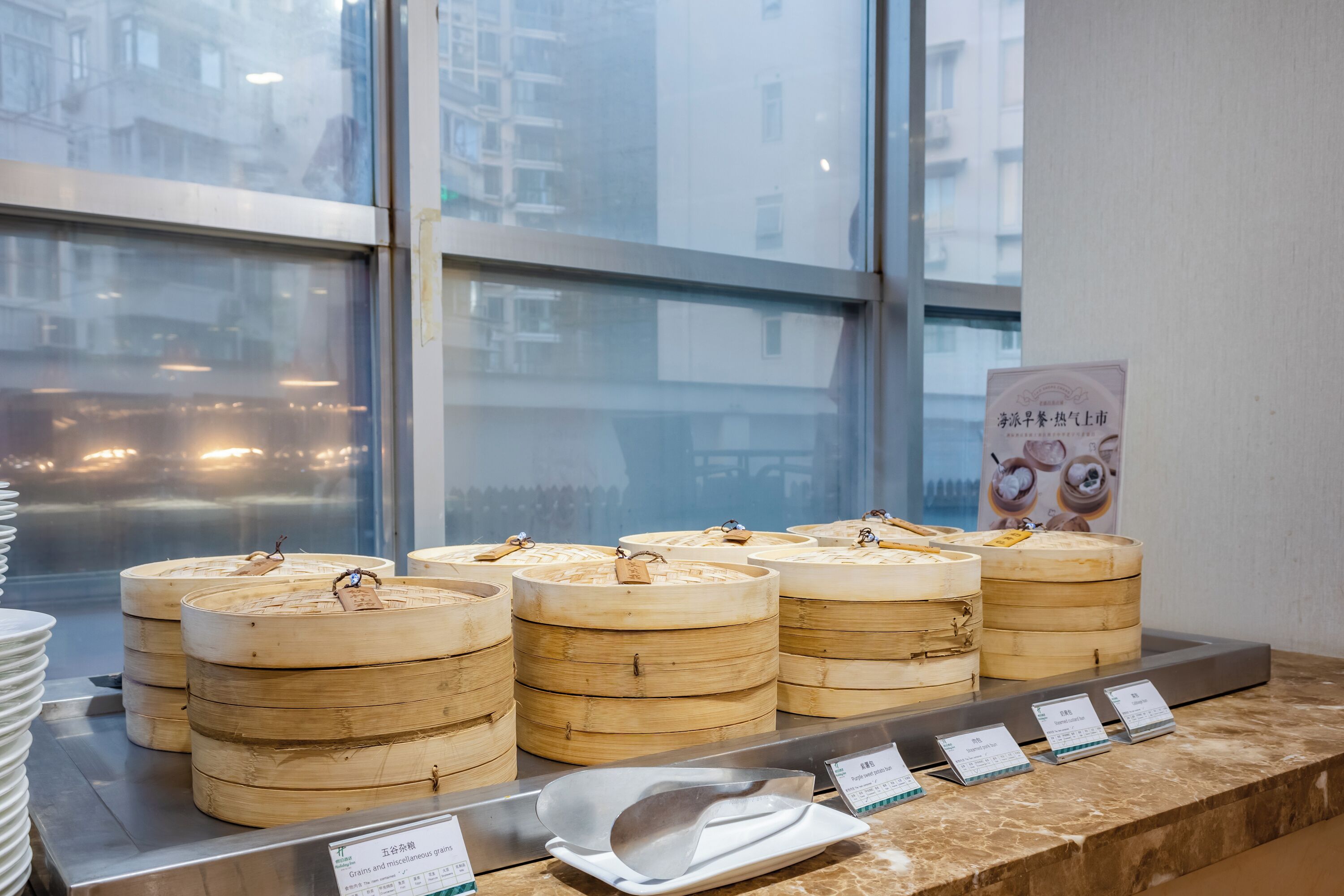 Una exhibición de recipientes de madera para calentar alimentos con etiquetas, apilados sobre una barra con vista a una ventana.