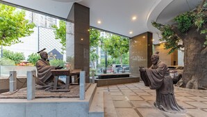 A statue of a scholar in a modern indoor setting with a large window and a tree. - Holiday Inn Vista Shanghai by IHG (Shanghai)