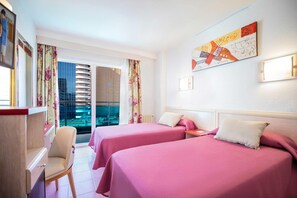 A hotel room with two beds, a desk, a chair, and a view of the city through the window. - Hotel Servigroup Venus (Benidorm)