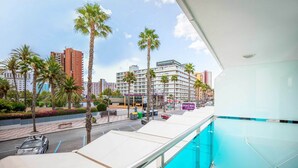 A hotel balcony with a pool, palm trees, and a view of the street and buildings. - Hotel Servigroup Venus (Benidorm)
