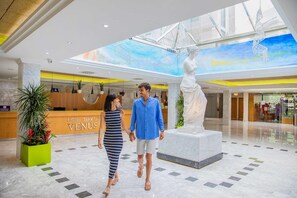 A hotel lobby with a reception desk, a large statue, and a high ceiling with a skylight. - Hotel Servigroup Venus (Benidorm)