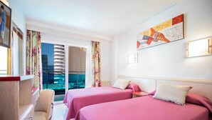 A hotel room with two beds, a desk, a chair, and a view of the city through large windows. - Hotel Servigroup Venus (Benidorm)