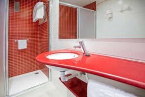 Un baño con un lavabo rojo, azulejos blancos, un espejo y una zona de ducha.