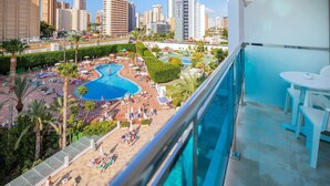 A hotel balcony with a pool area, including lounge chairs and umbrellas, and a cityscape view in the background. - Hotel Servigroup Venus (Benidorm)