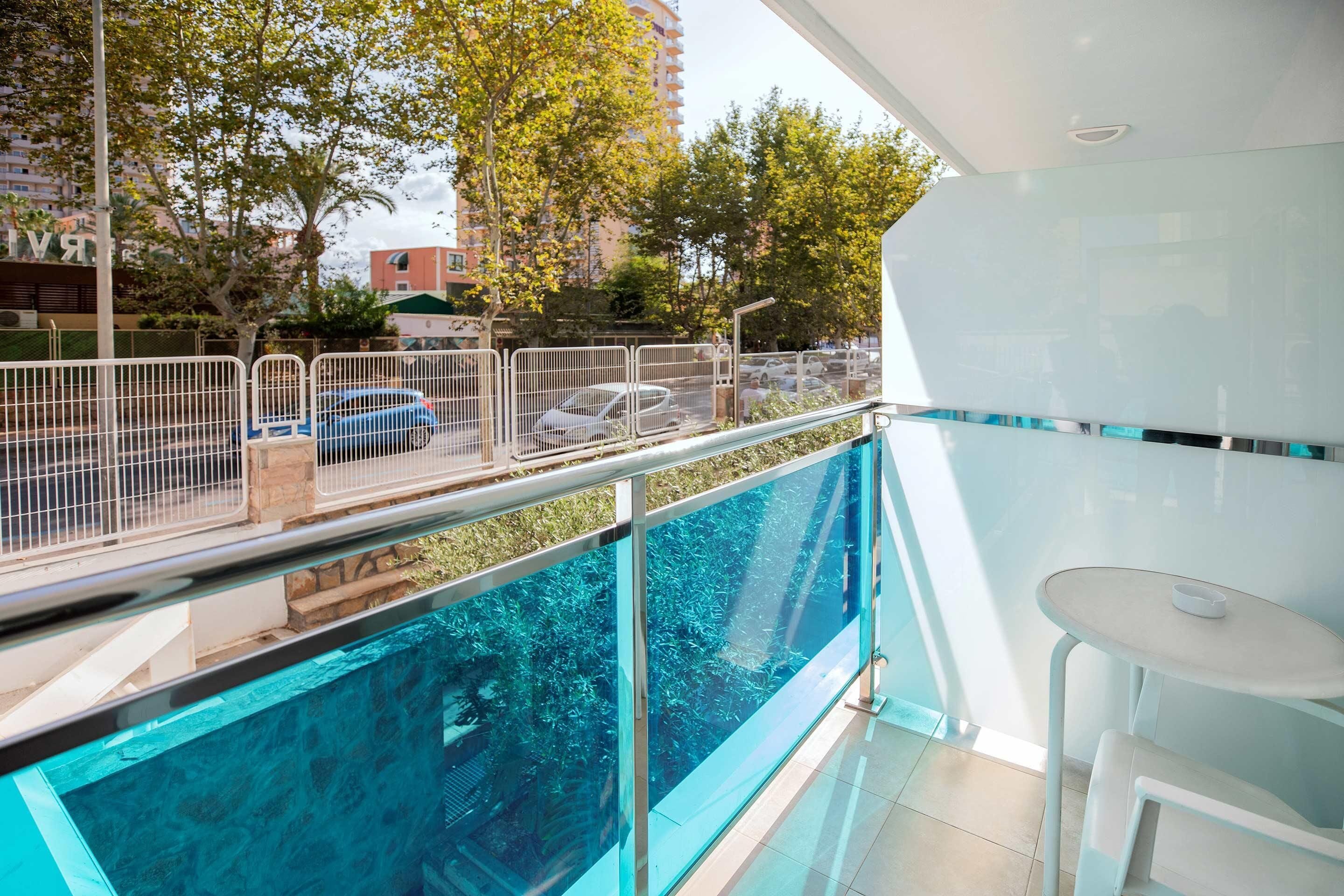 Un balcón moderno con baranda de vidrio que da a una piscina y vistas a la calle.