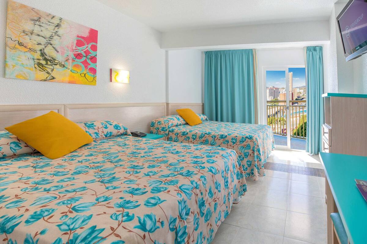 Habitación de hotel con dos camas, televisión y balcón con cortinas.