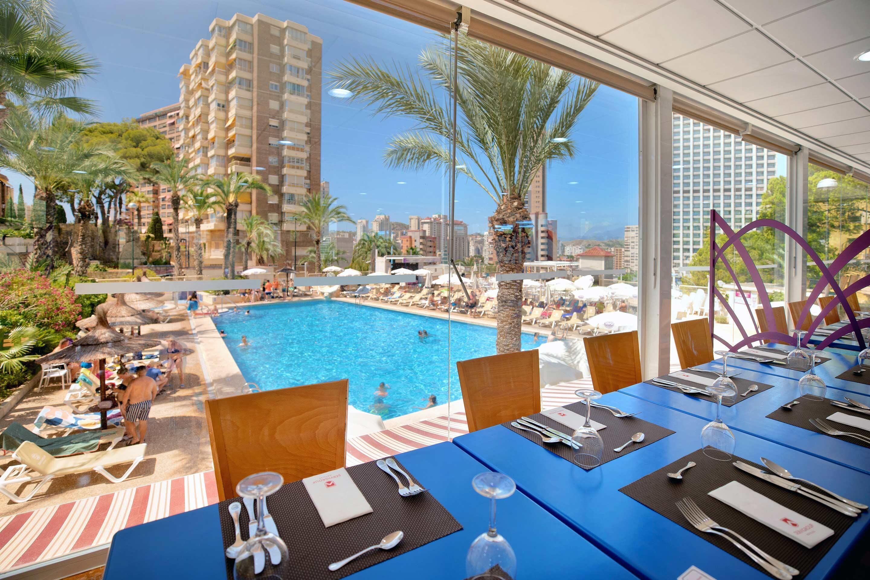 A dining area with tables set for a meal, overlooking a swimming pool and palm trees.