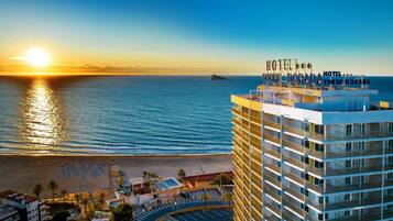 A hotel with multiple floors, a rooftop terrace, and a view of the sea and sunset.