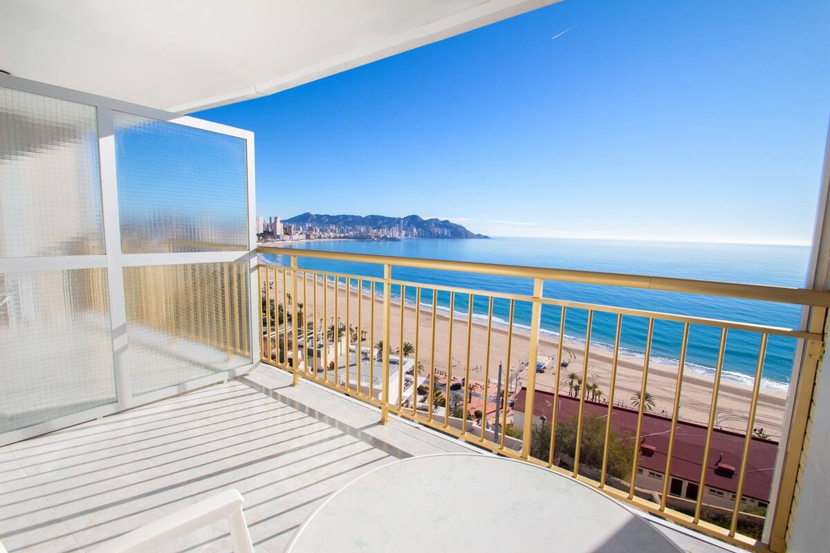 Un balcón con vista a la playa y un horizonte urbano distante.