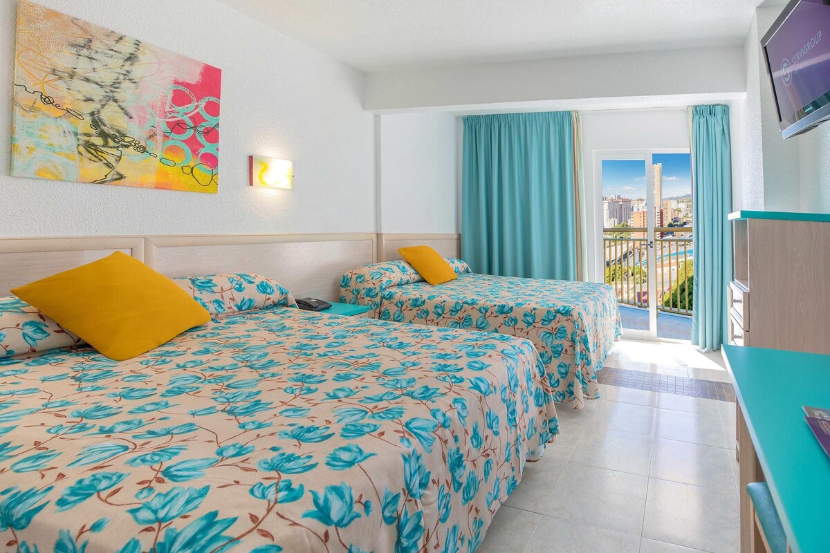 A hotel room with two beds, a TV, and a balcony with curtains.
