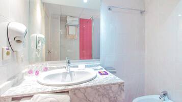 Un baño con lavamanos de mármol, ducha de mano, toallero y un bidé.