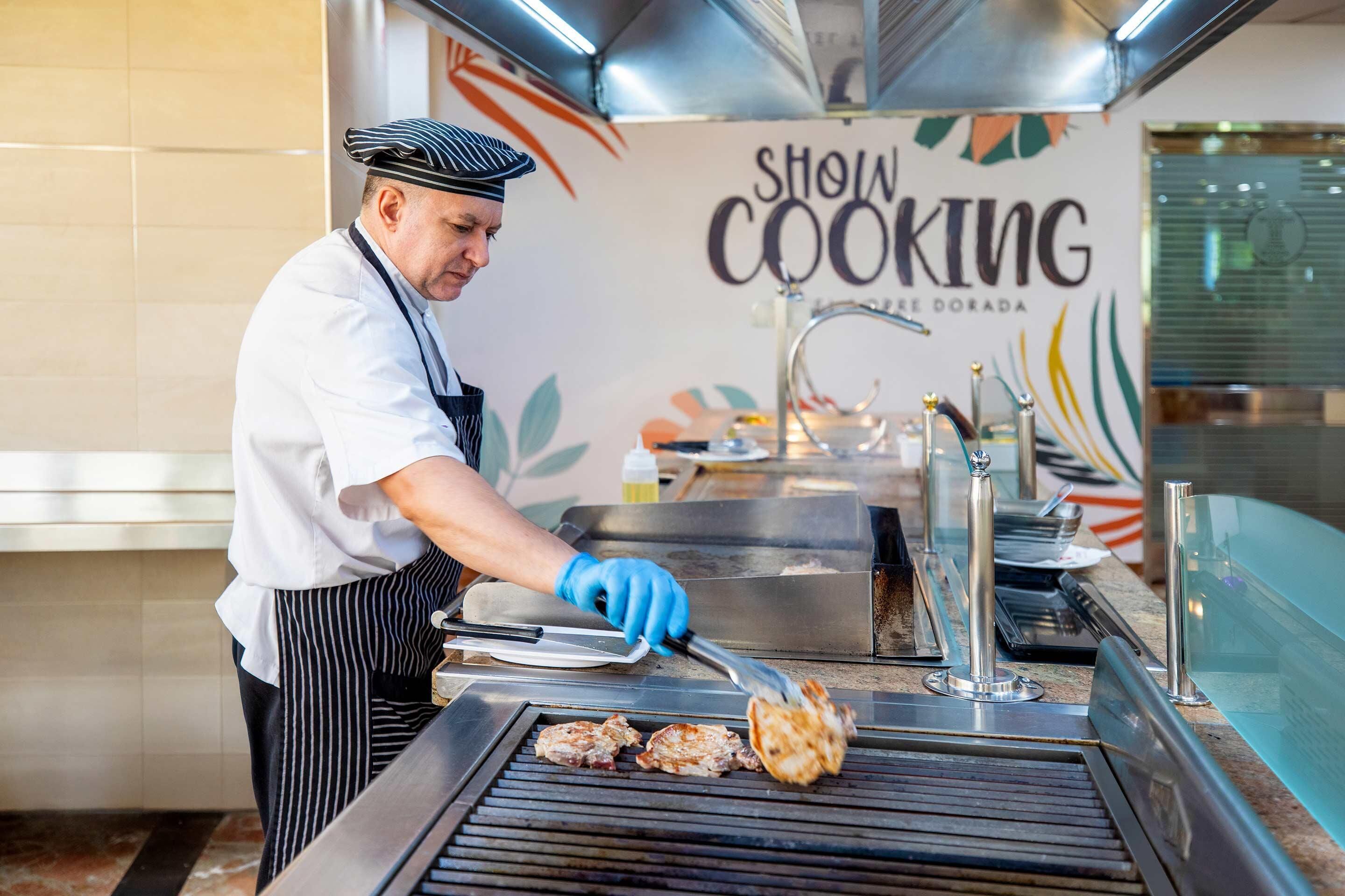 Un cuiner graella carn en una graella professional a la cuina, amb un cartell de 'Show Cooking'.