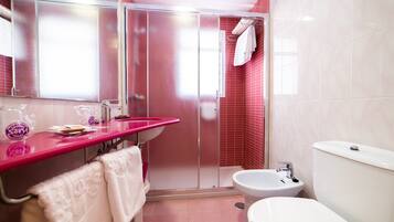 A bathroom with a pink vanity, a shower, a toilet, and a bidet.