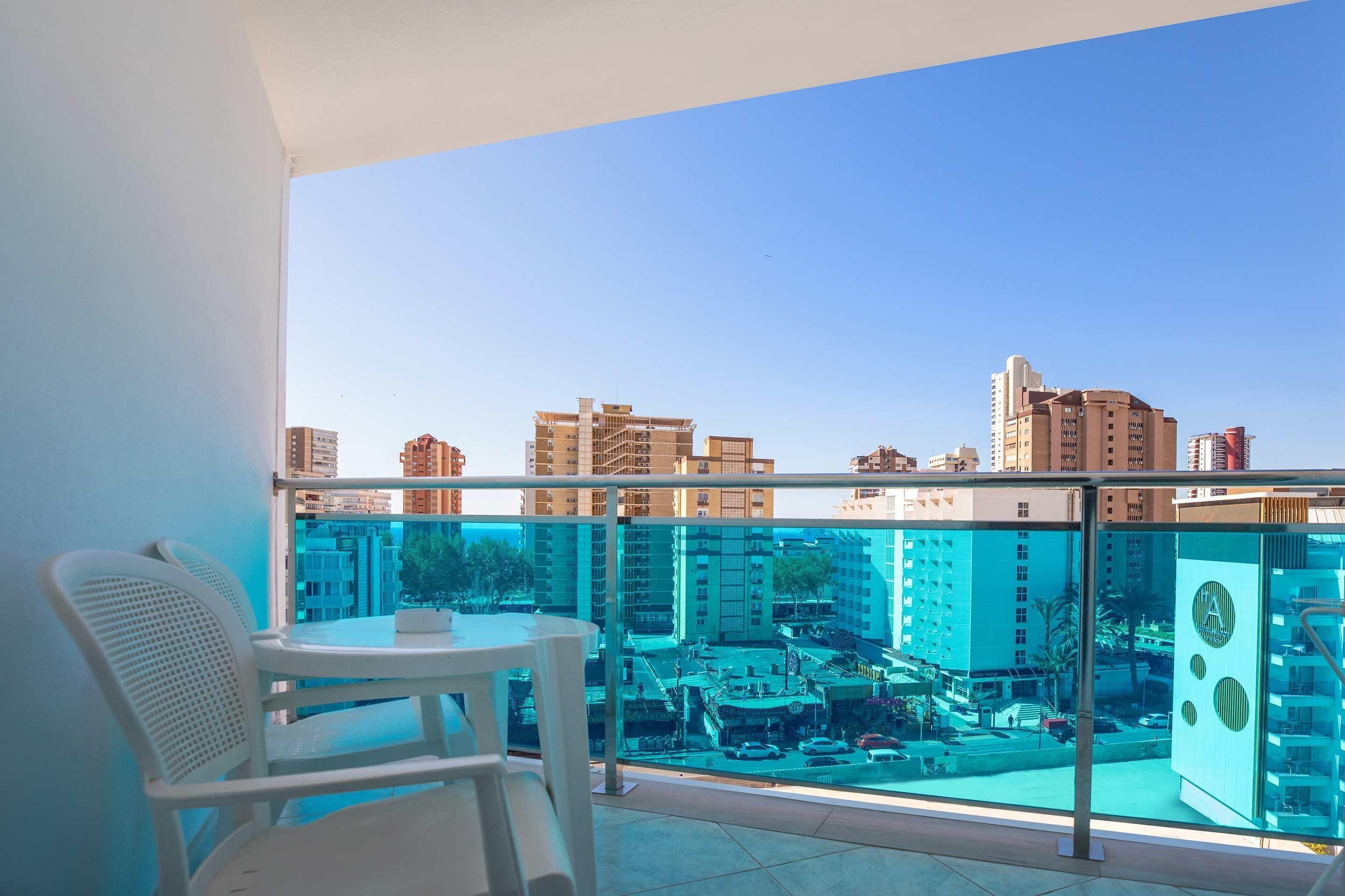 A balcony with a glass railing, a white chair, and a table.