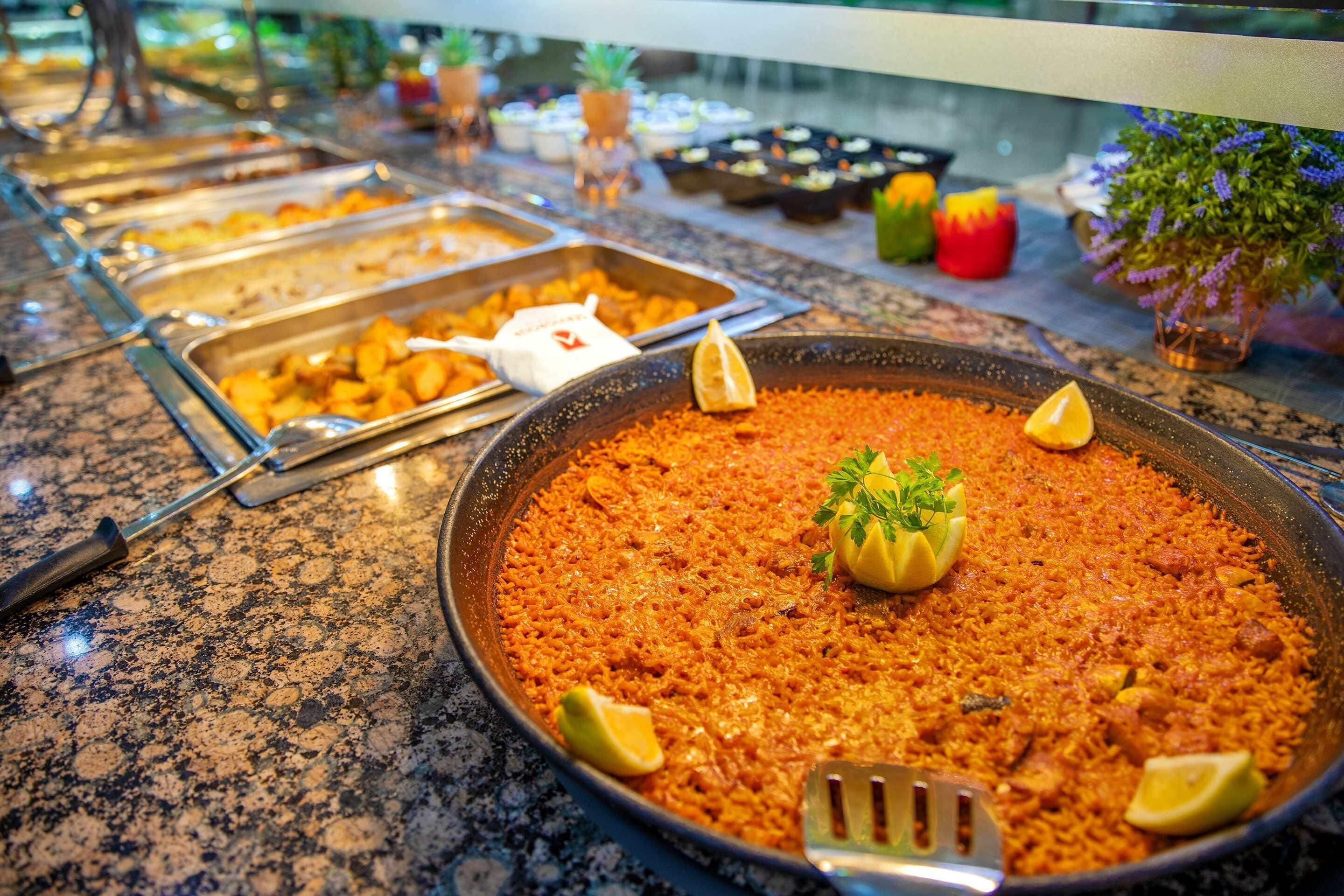 A buffet with various food options, including a large pan of rice garnished with lemon wedges and parsley.