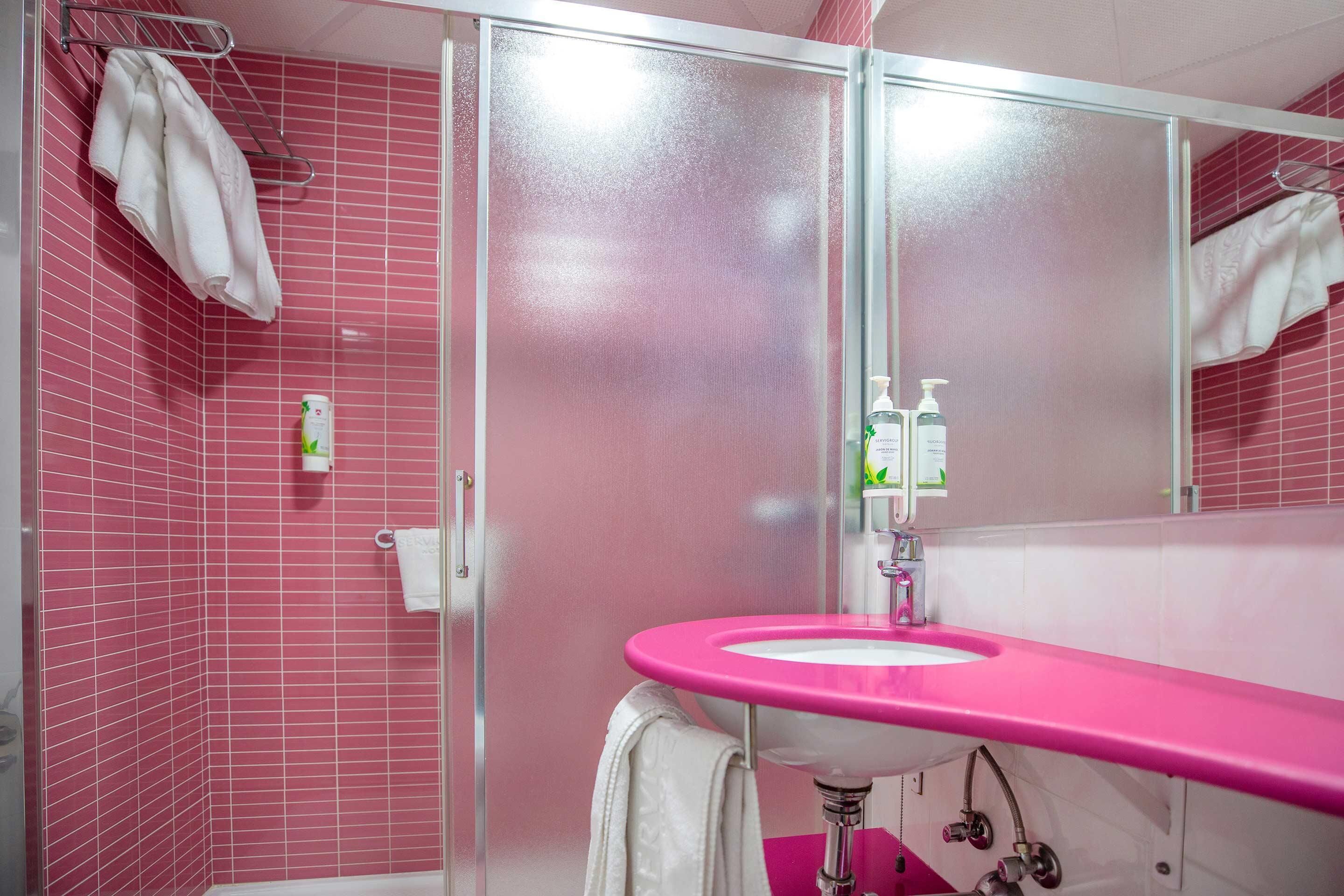 Ein Badezimmer mit rosa gefliesten Wänden, einem rosa Waschbecken und einer Duschkabine aus Glas.