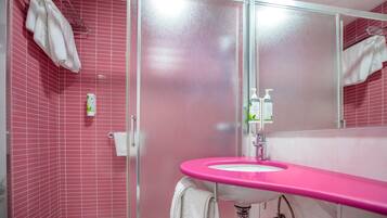 Ein Badezimmer mit rosa gefliesten Wänden, einem rosa Waschbecken und einer Duschkabine aus Glas.