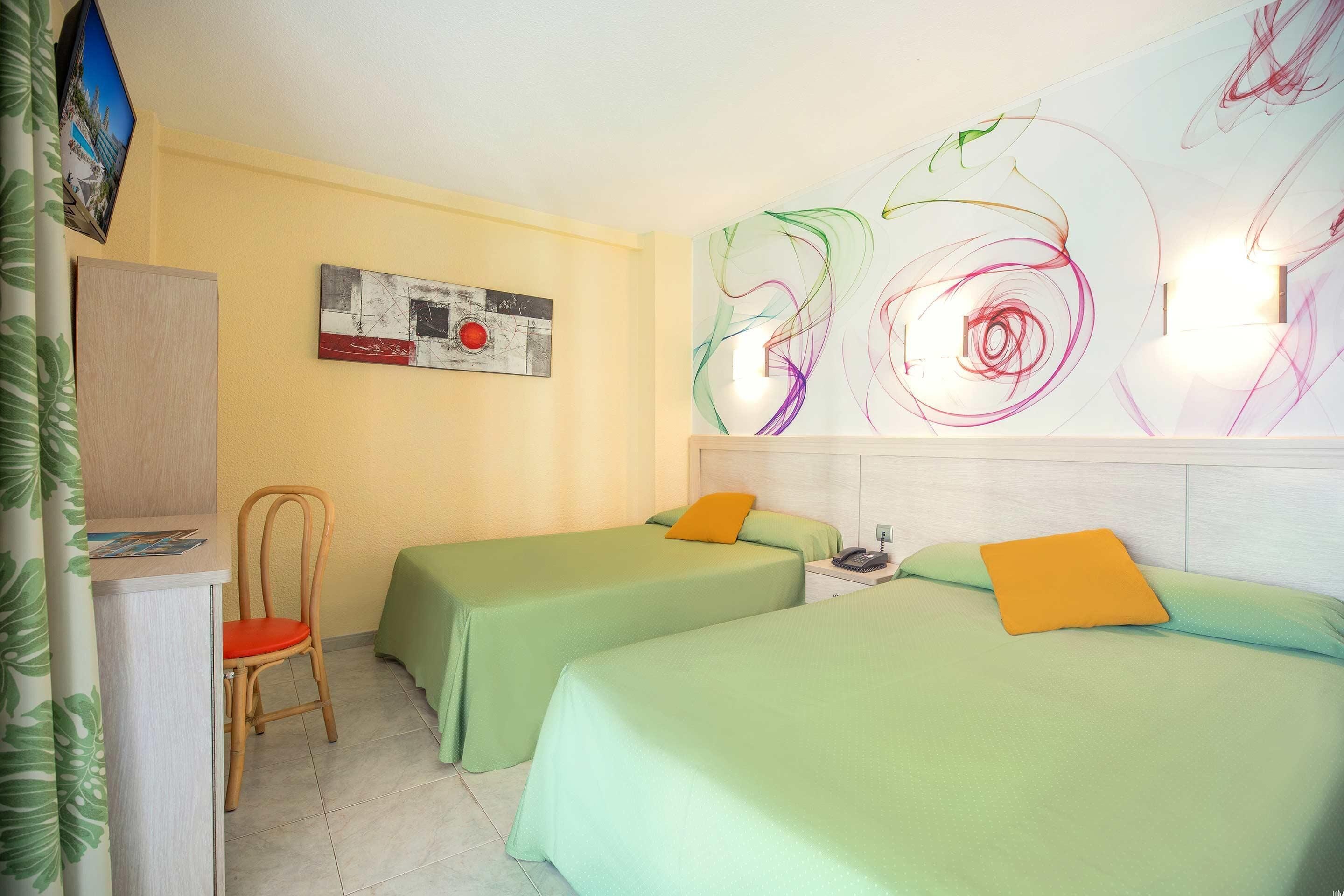 A hotel room with two beds, a desk, a chair, and a wall art piece.