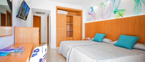 Habitación de hotel con dos camas, un armario de madera, un escritorio con silla y una obra de arte abstracta y colorida en la pared.