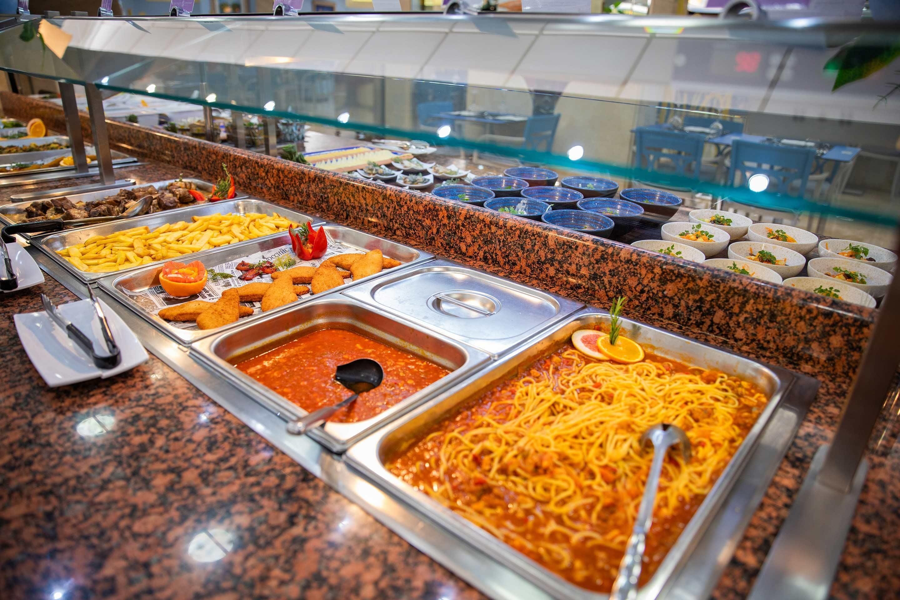 A buffet with various food options including pasta, French fries, and different sauces.