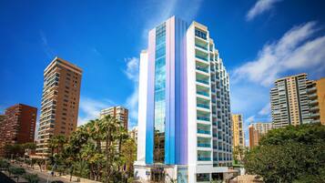 A modern high-rise hotel with a prominent vertical blue and white facade, surrounded by palm trees and other buildings.