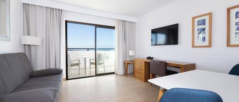 A modern hotel room with a balcony, a sofa, a desk, and a TV.