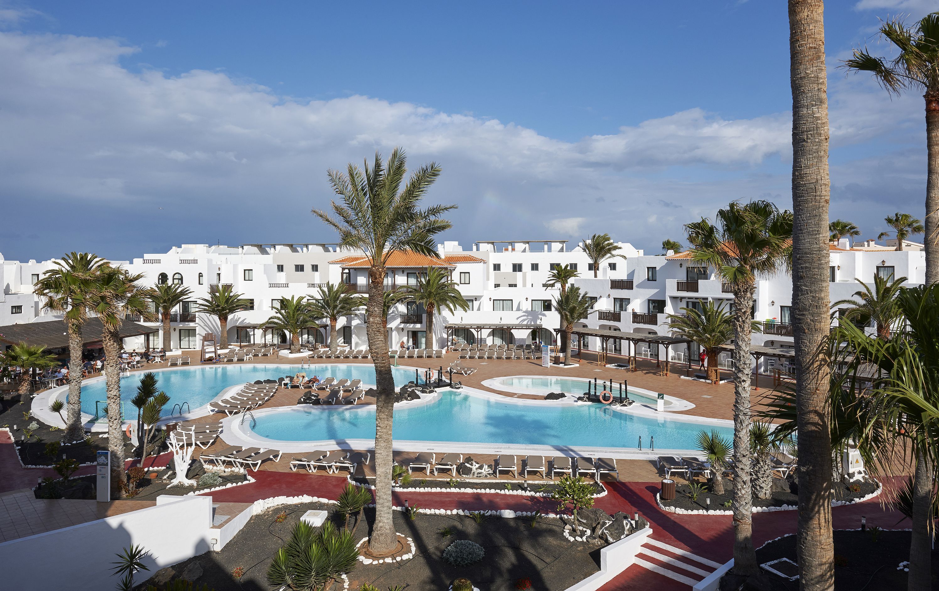 Un resort con varias piscinas, palmeras y edificios blancos.