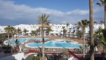 Resort com várias piscinas, palmeiras e edifícios brancos.