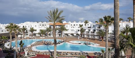 Un resort con varias piscinas, palmeras y edificios blancos.