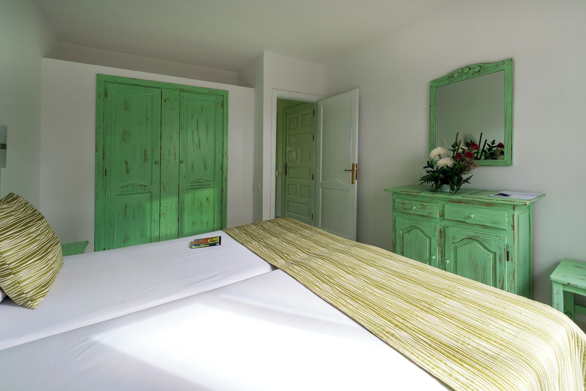 A room with a bed, a green dresser, a mirror, and a door.