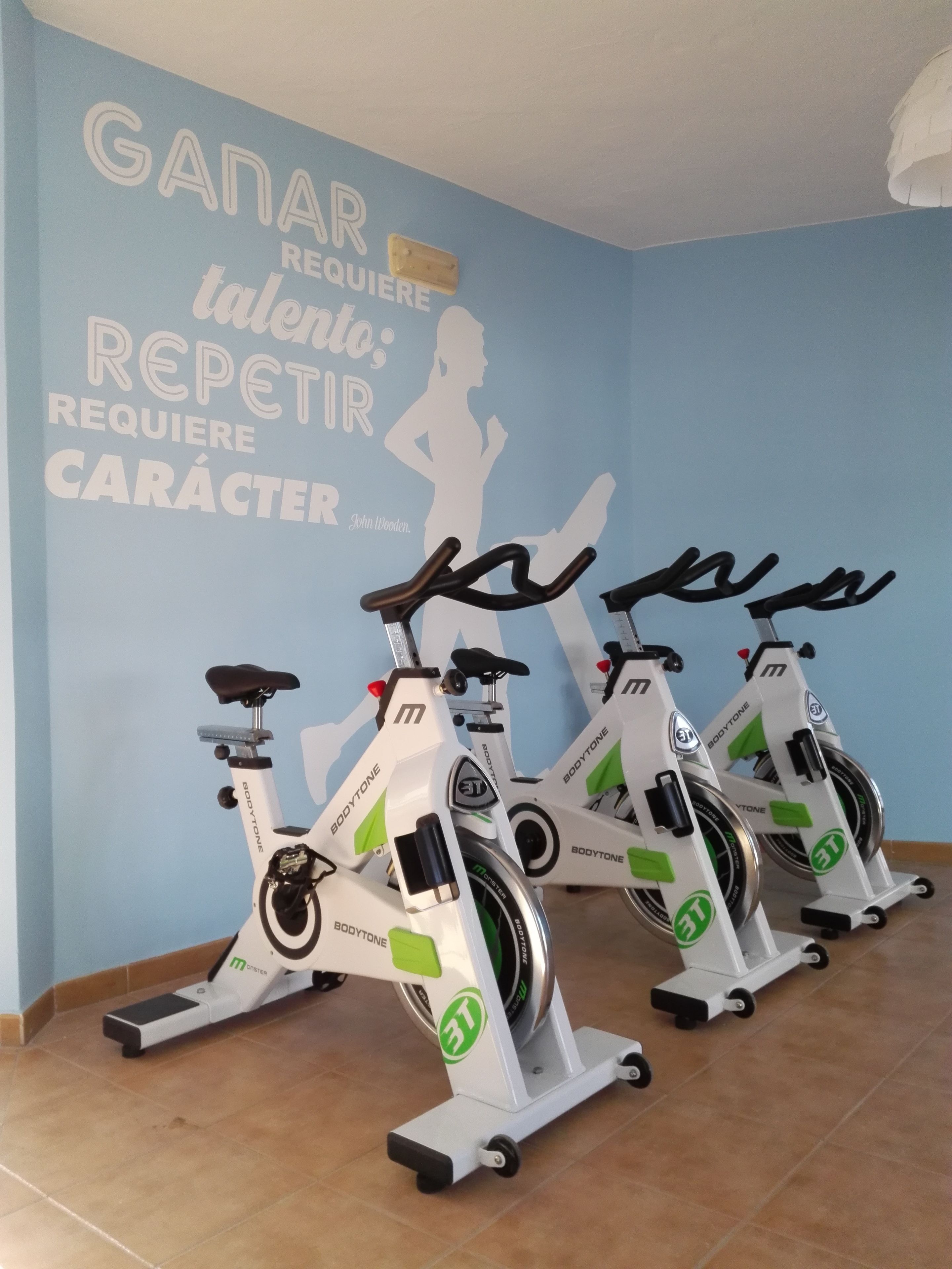 Tres bicicletas estáticas en una habitación con pared azul y texto motivacional.
